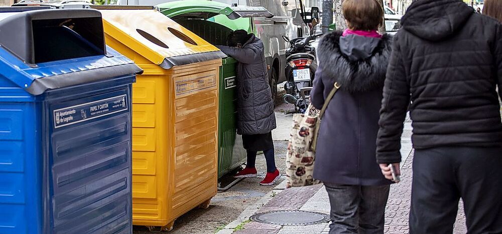 Una mujer rebusca en un contenedor de basura.