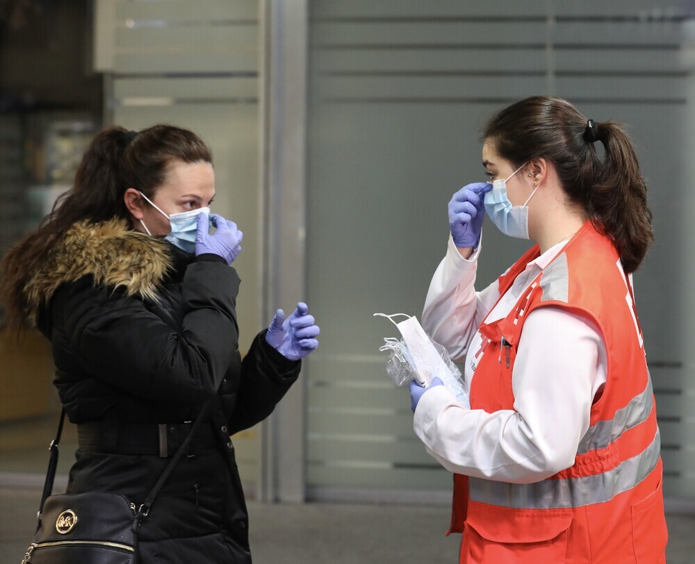 Una voluntaria de Cruz Roja da indicaciones a una pasajera sobre cómo ponerse una mascarilla en la estación de Cercaní­as de Atocha.